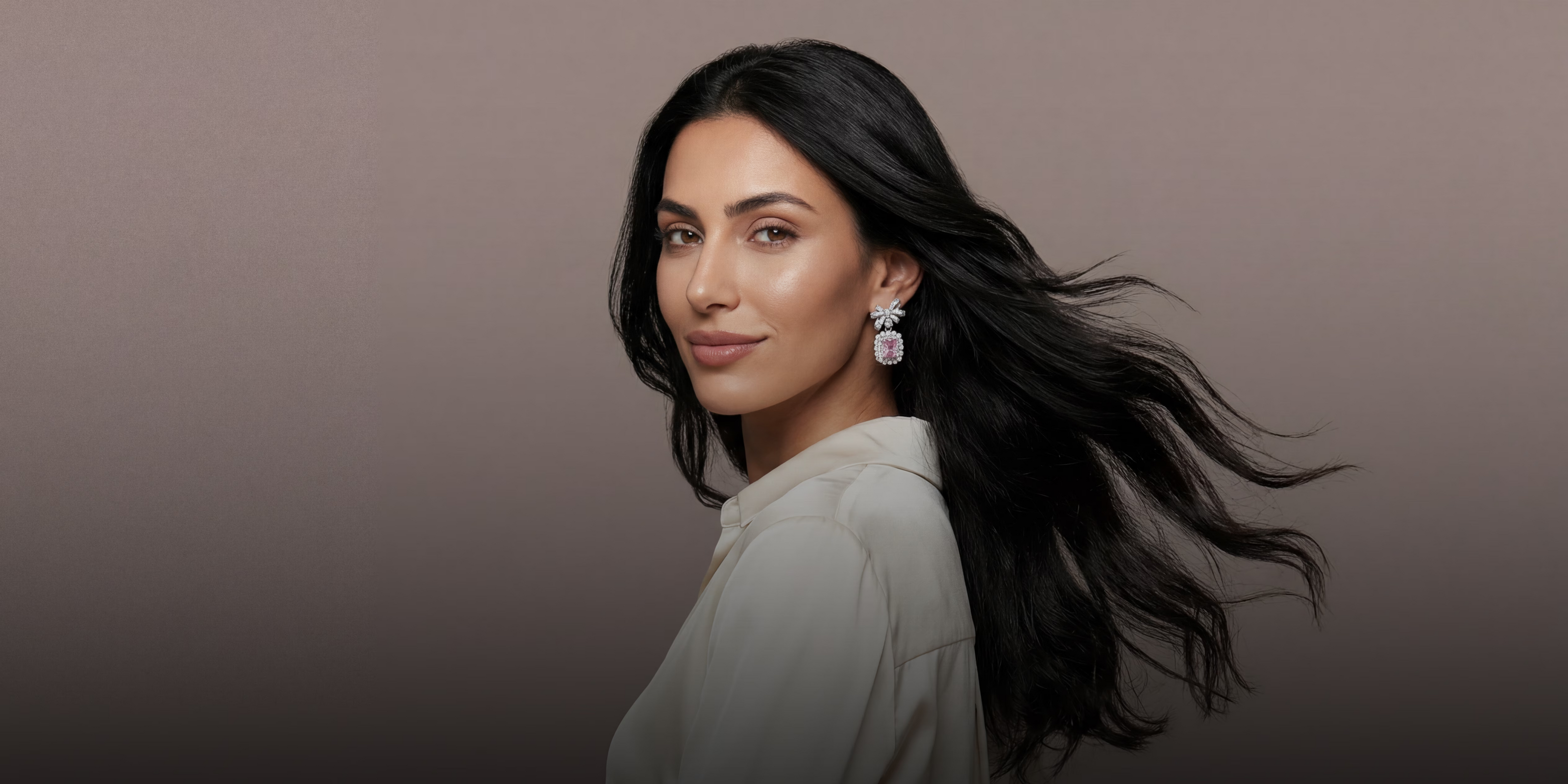 Woman with flowing hair wearing an earring with a pink gemstone against a neutral background